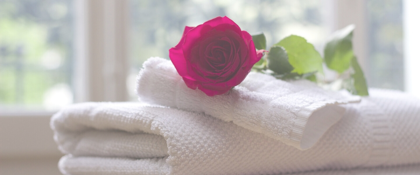 投稿記事のイメージ写真。白い畳んだバスタオルの上に白い畳んだタオルが置かれ、その上にピンクの薔薇の花が置かれています。
