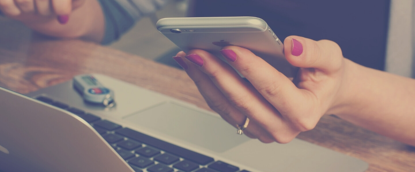 RESERVEのイメージ写真。机に置かれた開いたシルバーのパソコンと、机の椅子に座った人の左手に持ったシルバーのiPhone